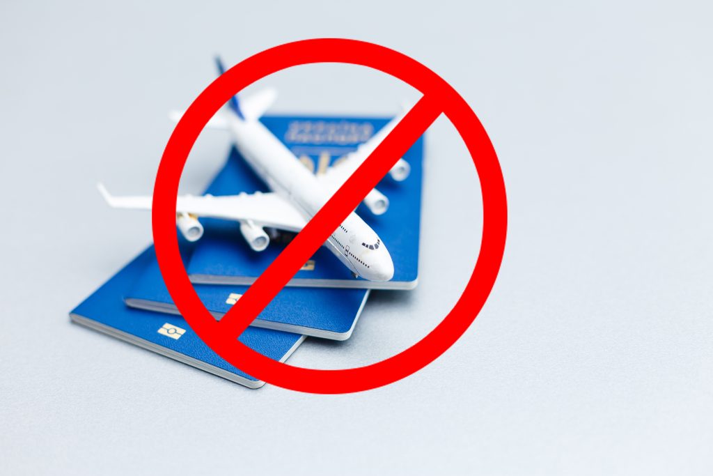 a pile of passport and over them a toy aeroplane with a no sign showing you cannot travel.