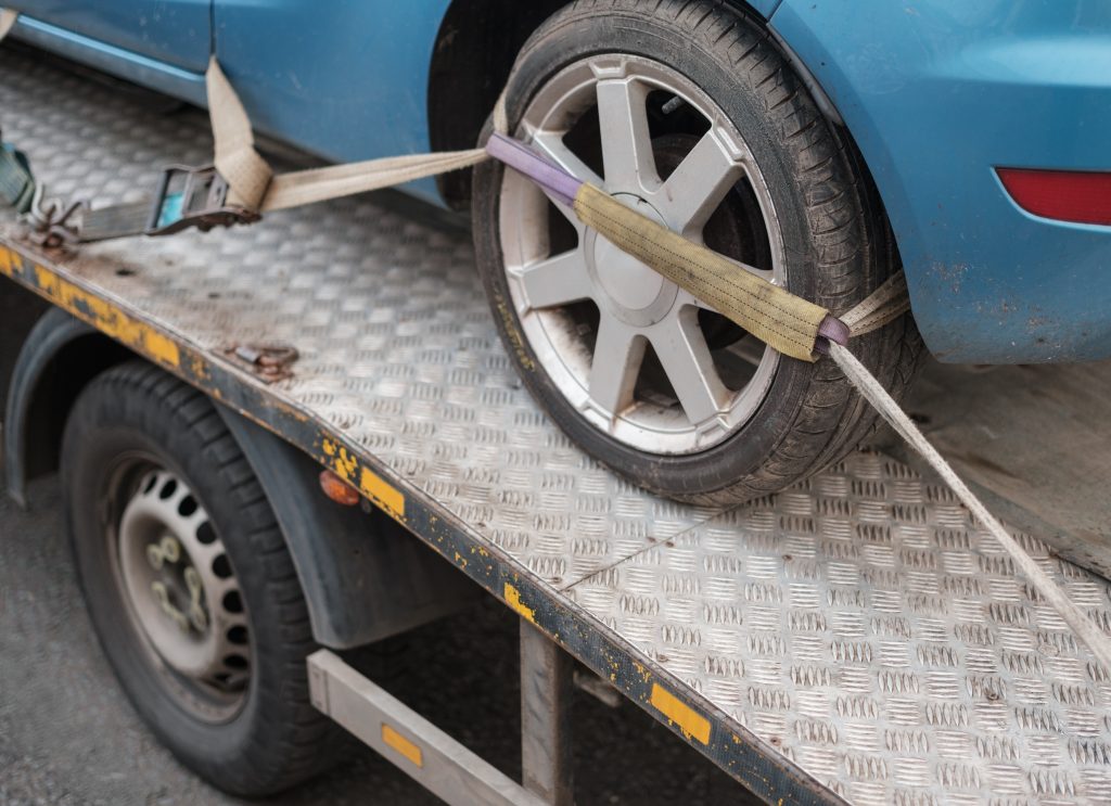 A blue car wheel tied with a rope on a recovery truck