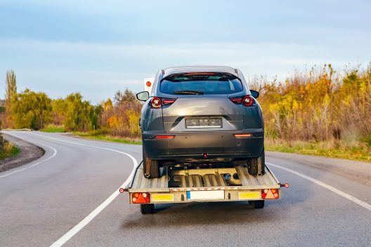 A damaged car on a recovery truck going on a two lane road.